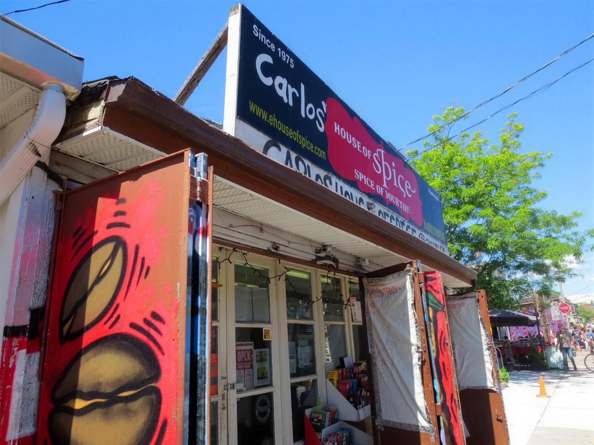 The storefront of Carlos' House of Spice at 190 Augusta Ave: printed banner overhead, graffiti-painted shutters below